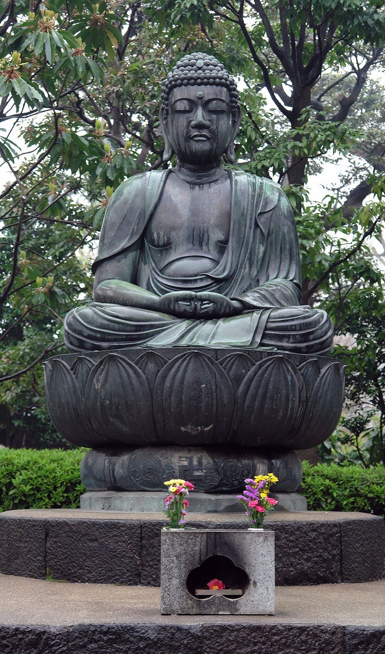 Statue de Bouddha dans un jardin japonais paisible, symbolisant la tranquillité et la pleine conscience.