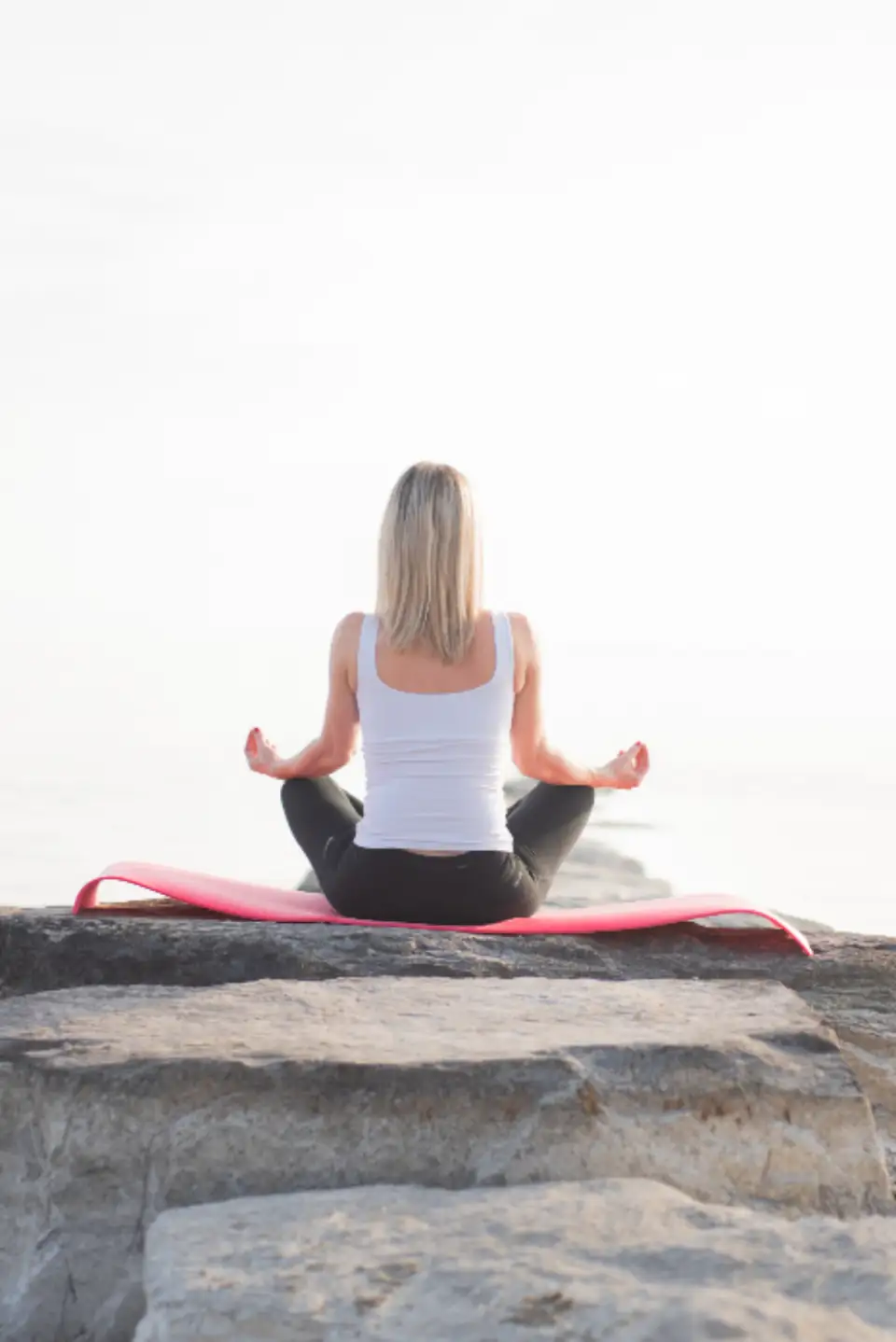 Jeune fille qui médite le dos tourné sur un rocher